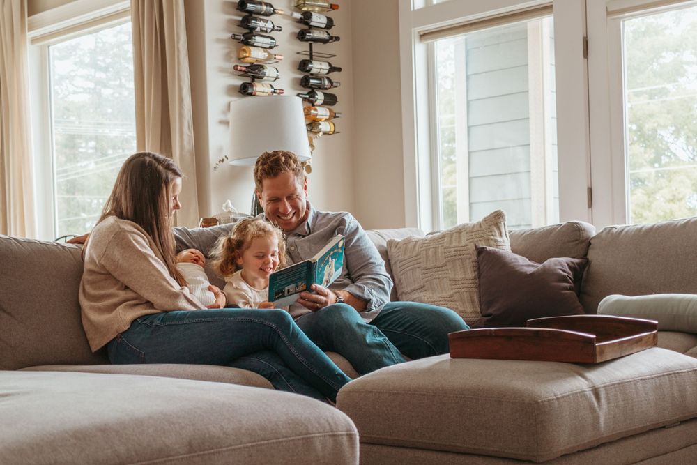 Casual family gathering on sectional sofa in bright living room with large windows.