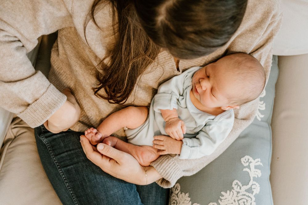 Overhead view of baby in light blue outfit being held on white bedding.
