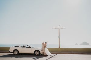 Pareja junto a un Mustang blanco frente al mar en Mazatlán durante una sesión de boda al atardecer — Carlos Galindo Wedding Photographer