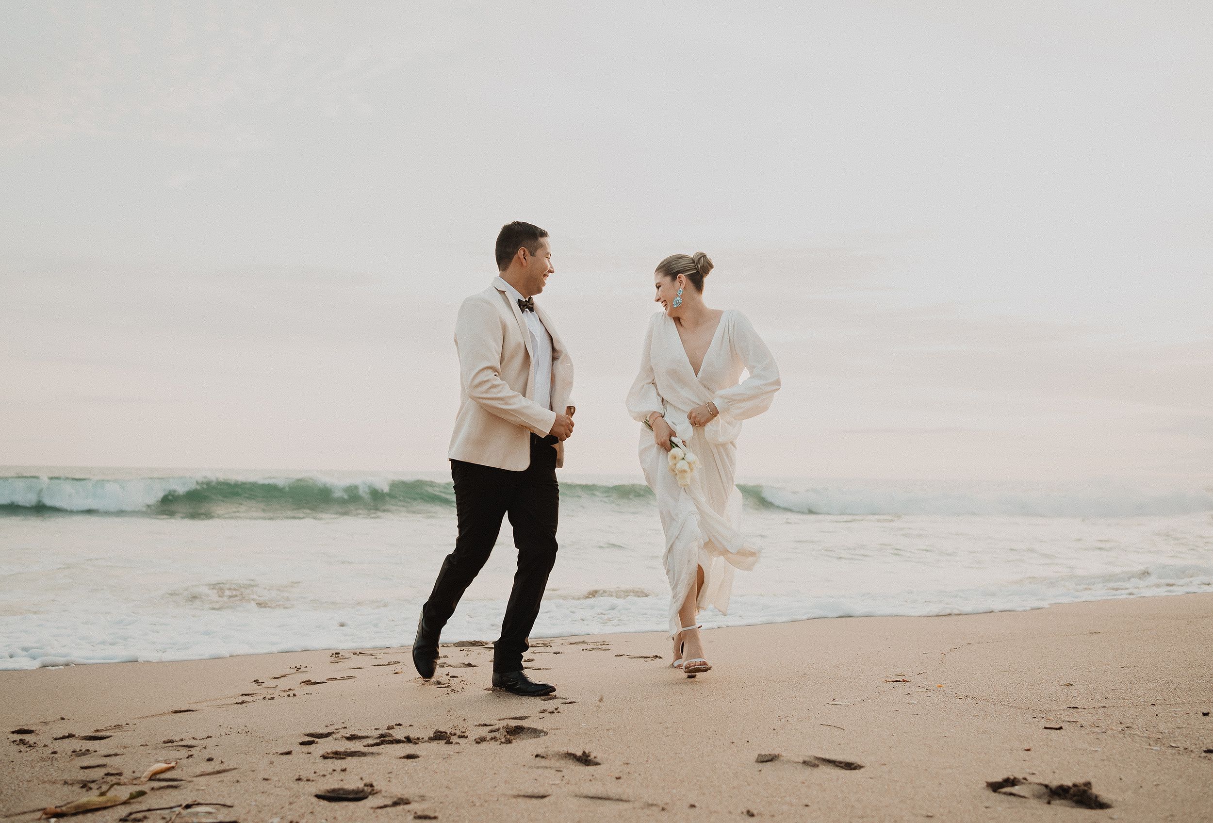 Pareja caminando y riendo en la playa durante una sesión al atardecer en Mazatlán, con un estilo natural y espontáneo.