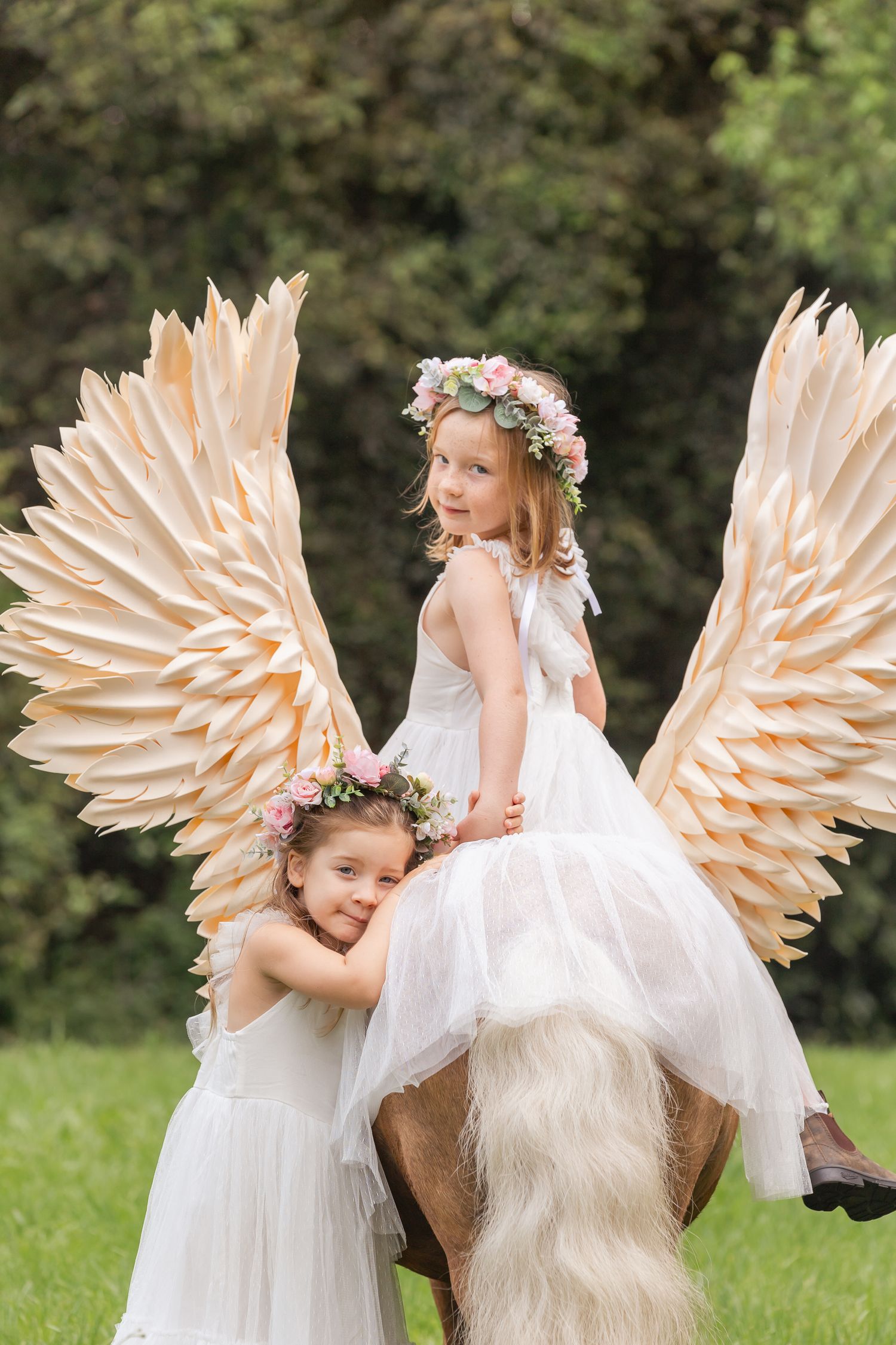 Dreamy photoshoot with decorative angel wings and white horse in a garden setting.