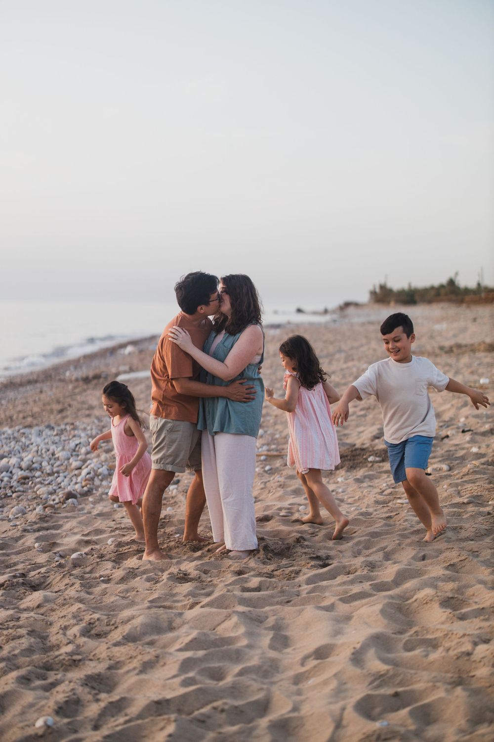 Family playing and embracing on a beach during golden hour.