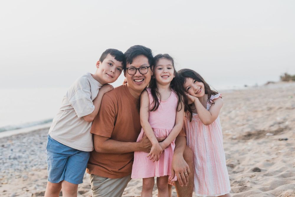 A happy family poses together on a beach with a misty sky backdrop.