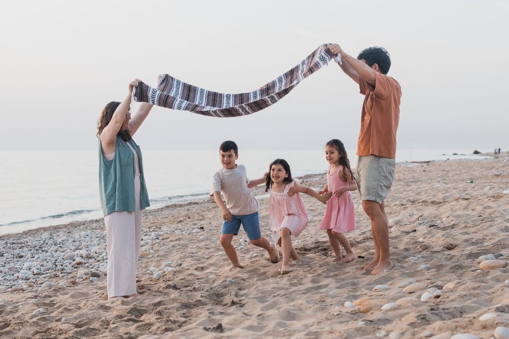 People playing under a blanket arch on the beach during sunset.
