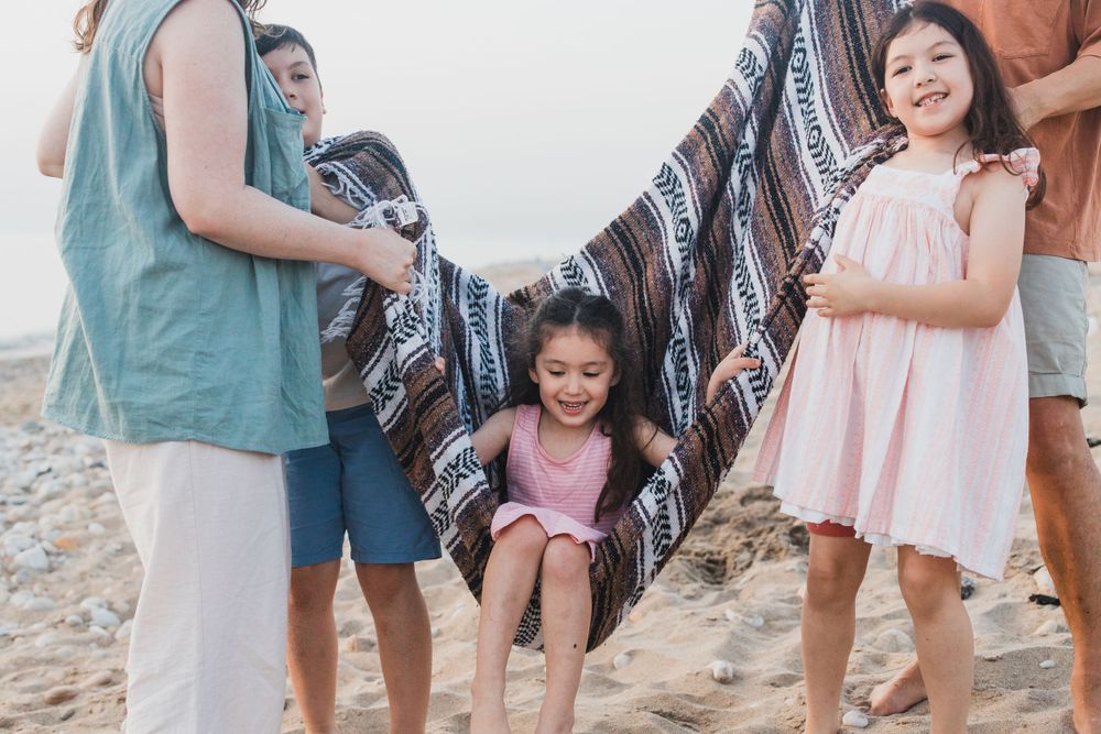 Children playing under a blanket held up by adults on a rocky beach.