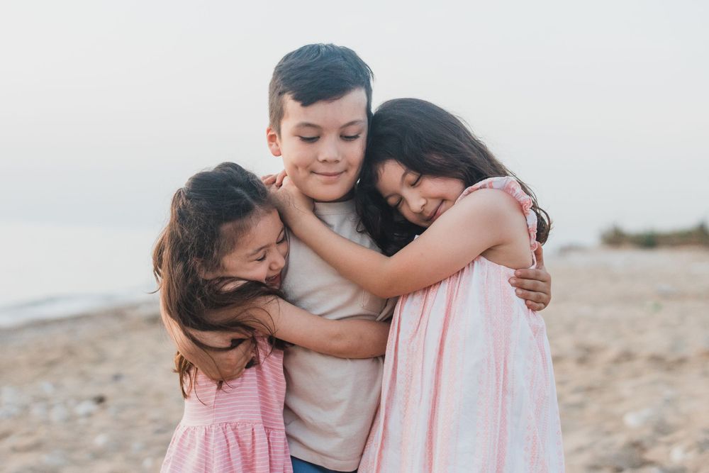 Three people sharing a warm group hug on the beach.