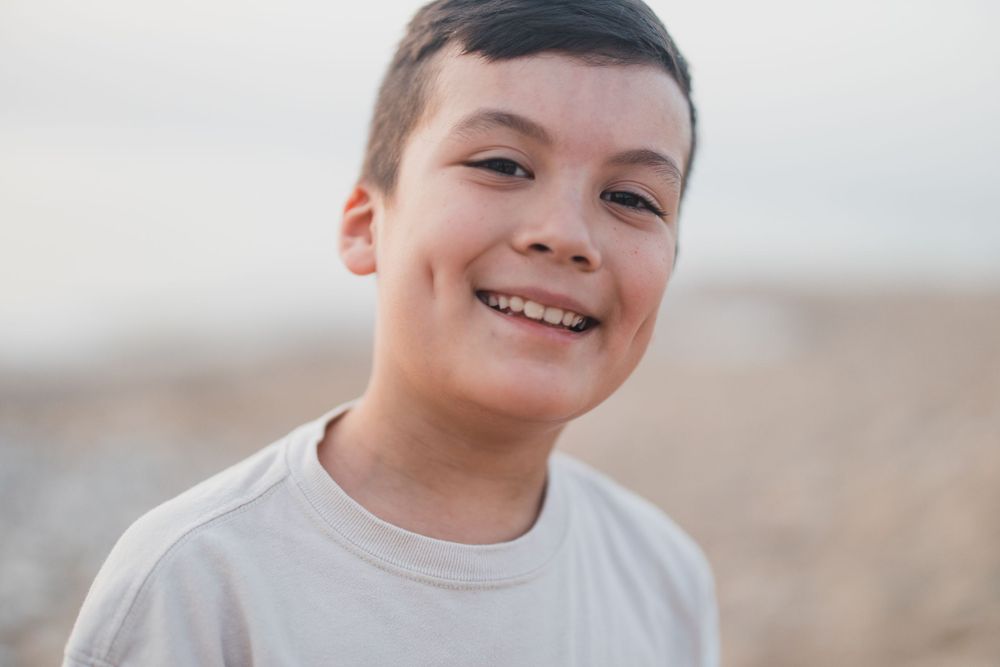A young person smiling joyfully against an overcast beach background.
