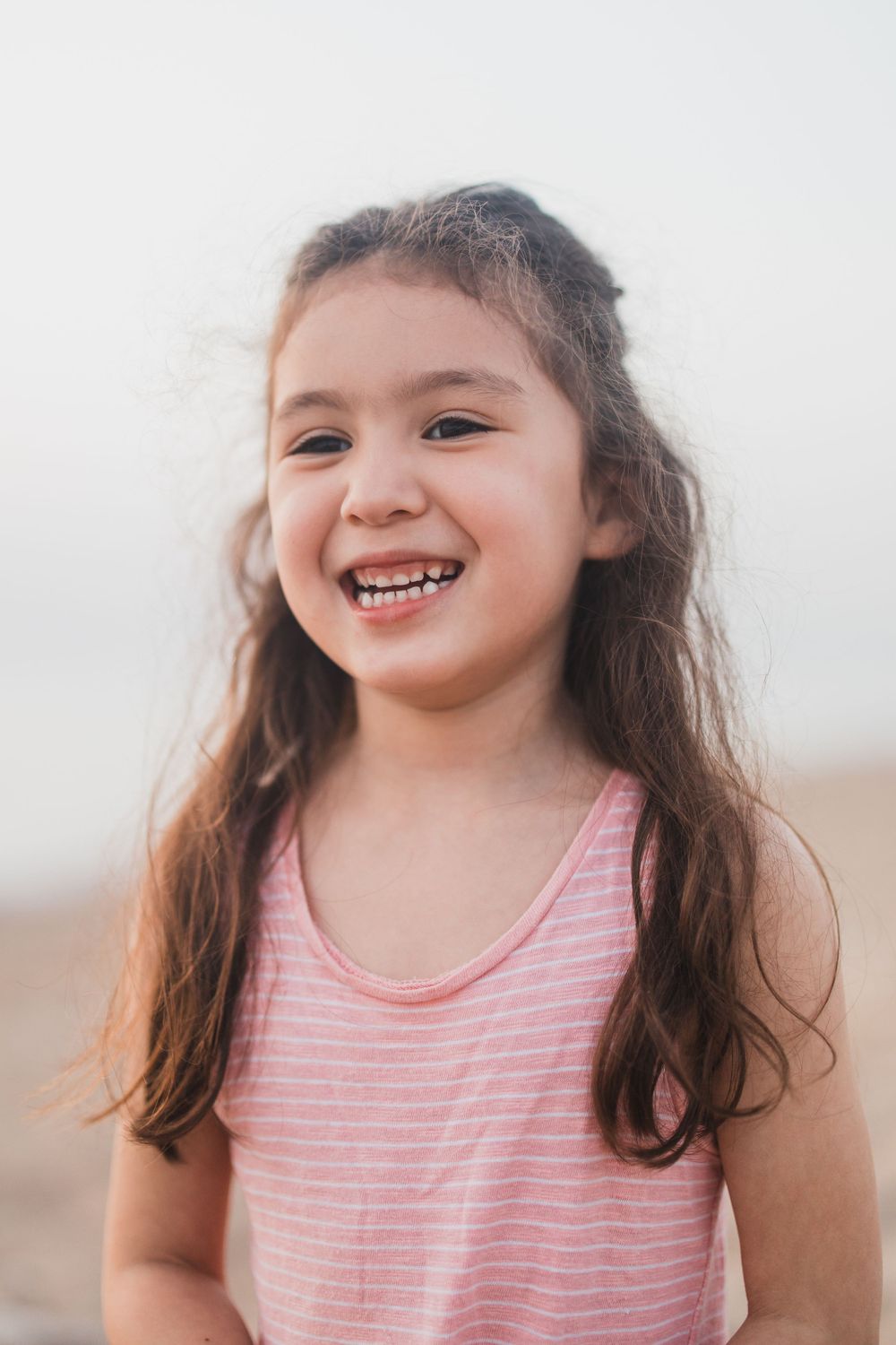 A young person in pink stripes laughs joyfully outdoors.
