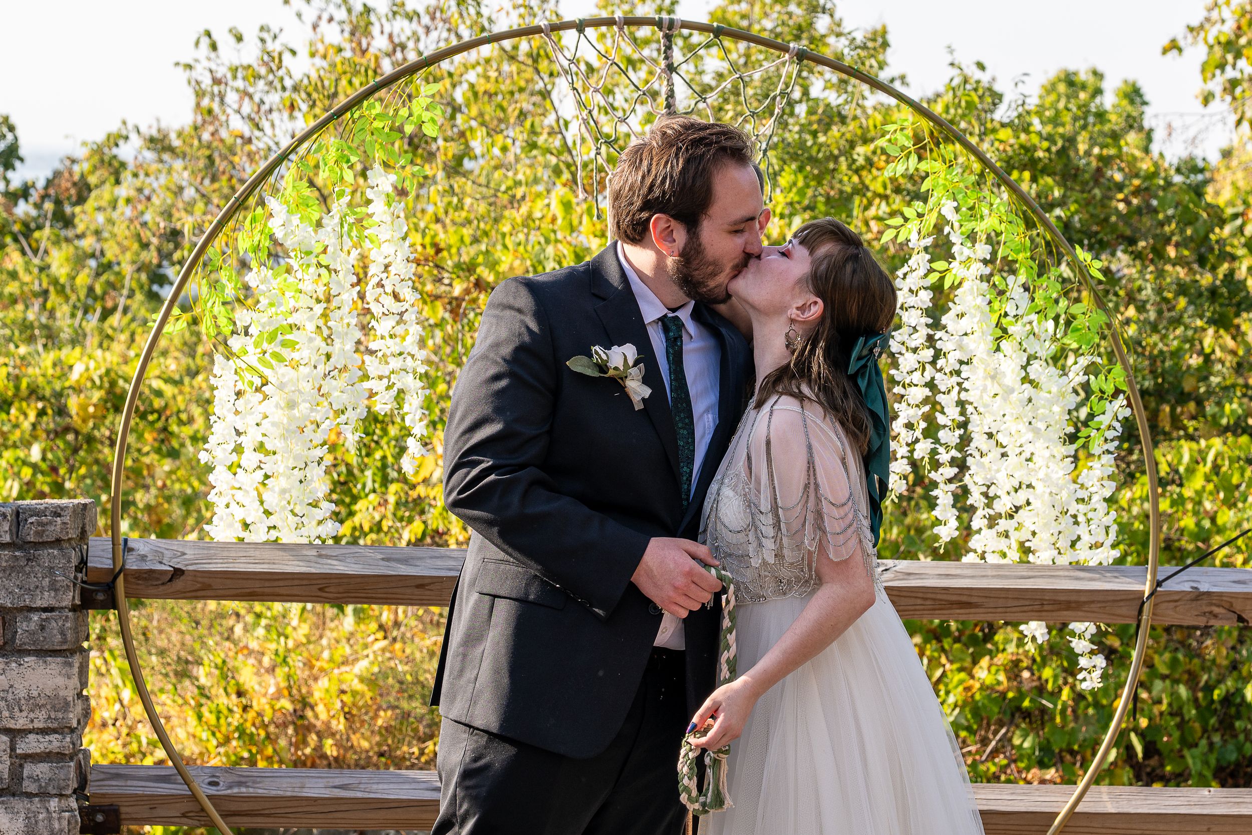 A bride and groom share an intimate forehead touch moment outdoors near a large tree, wearing white gown and blue suit.