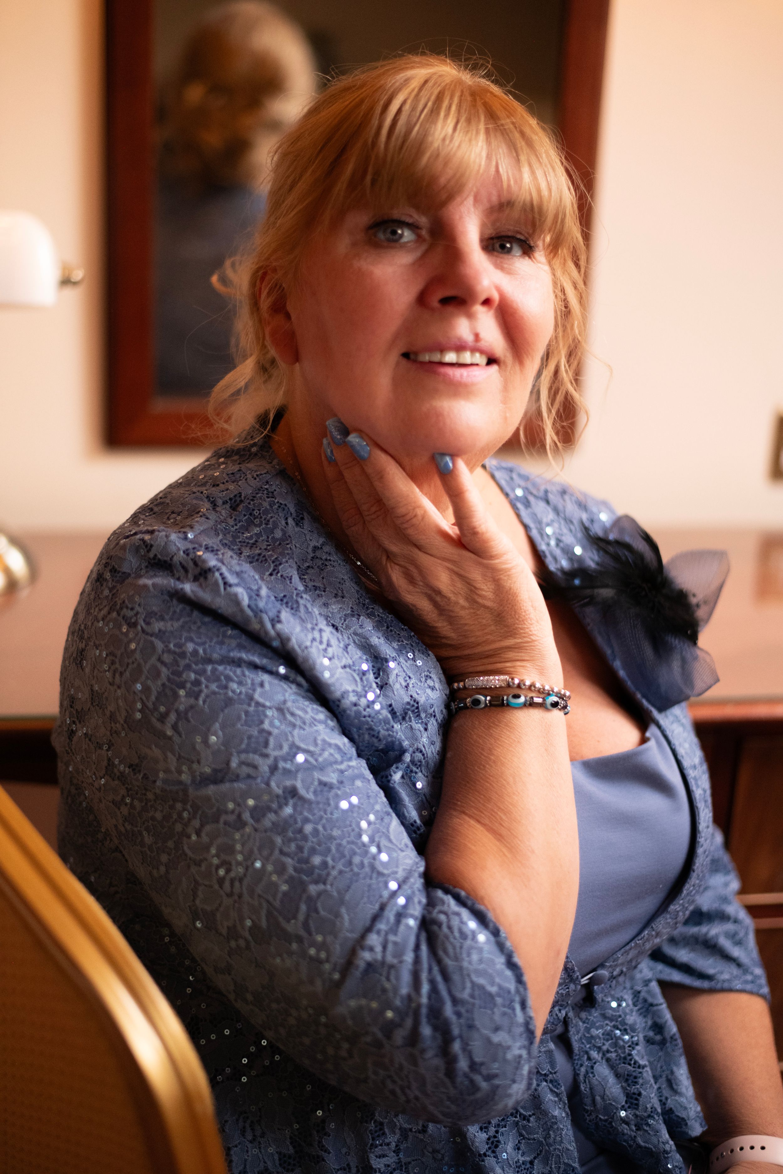 A woman in a blue dress smiles while touching her face during a formal event.