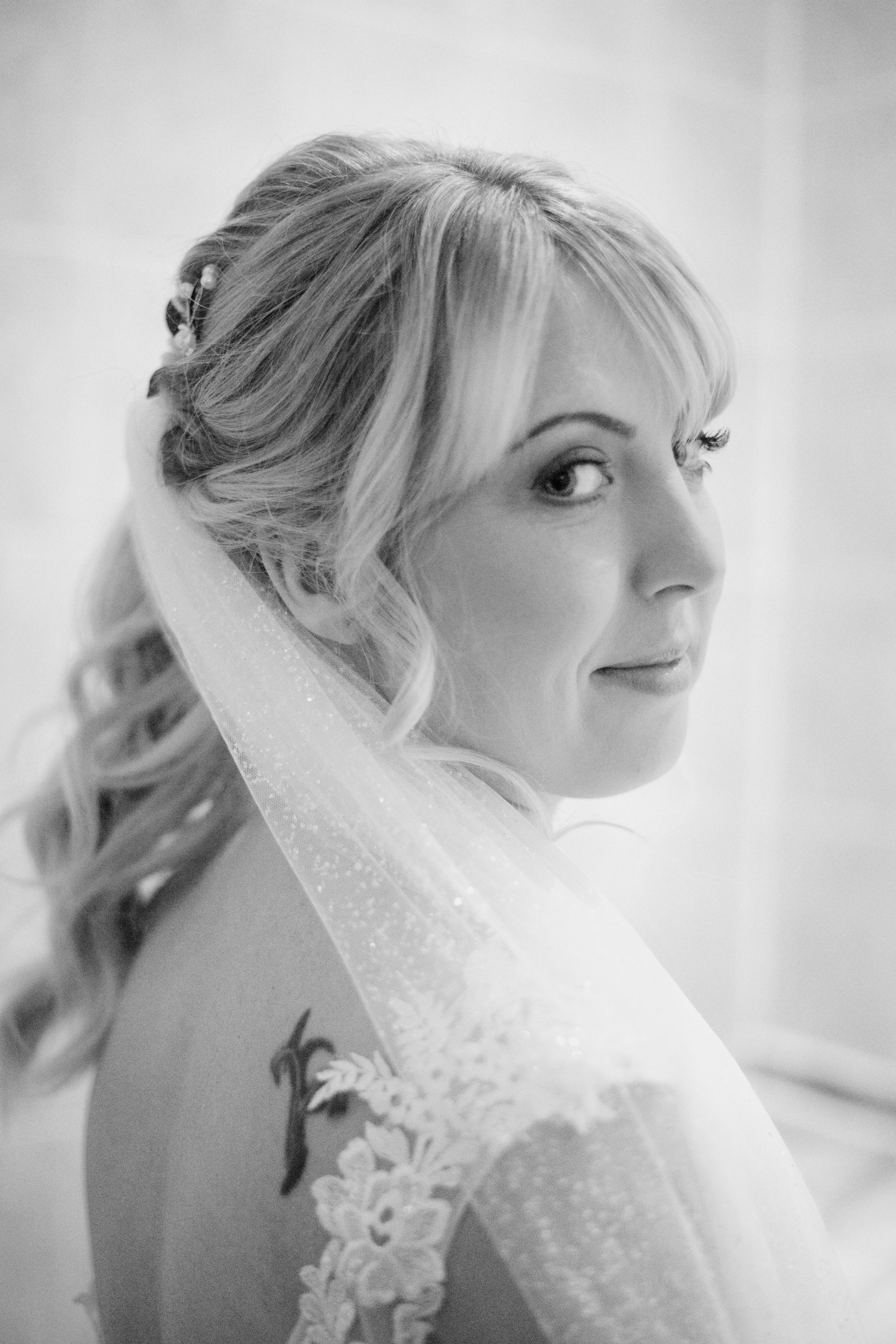 Side profile portrait of a bride wearing a delicate veil and lace dress.