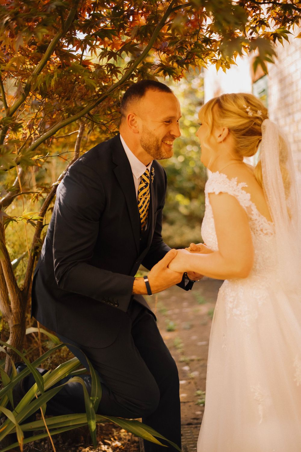 A couple shares a joyful moment under autumn foliage during their wedding.