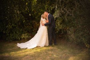 A couple shares a romantic moment in their wedding attire on a grassy lawn at dusk.