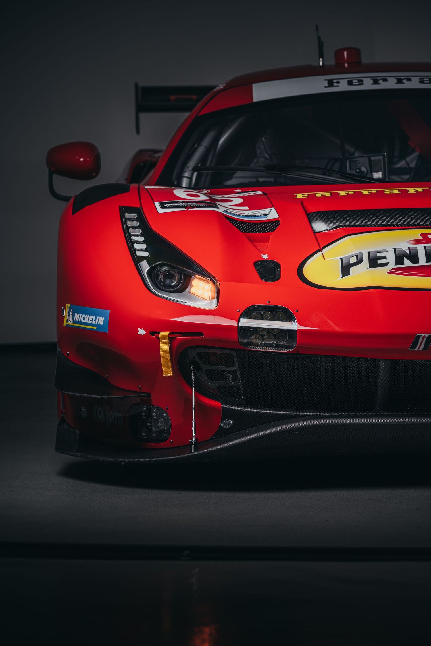 Close-up profile of red Ferrari race car with Pennzoil sponsorship in moody lighting.
