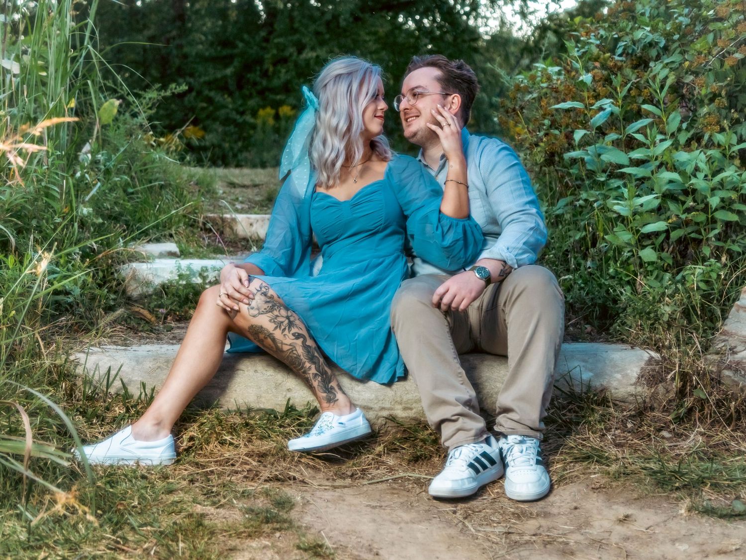 A couple sharing a playful moment while sitting on concrete steps surrounded by greenery.