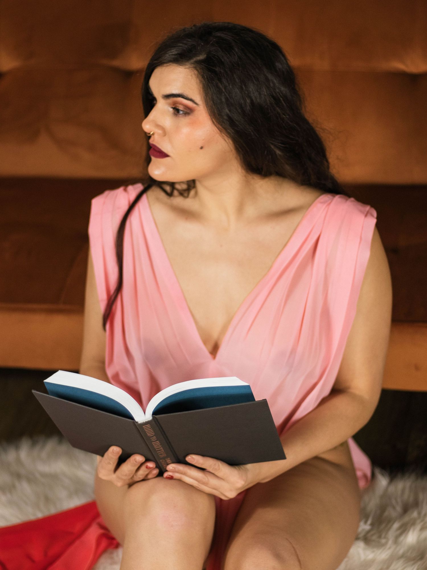 A portrait of someone in a pink dress reading a book on a brown couch.