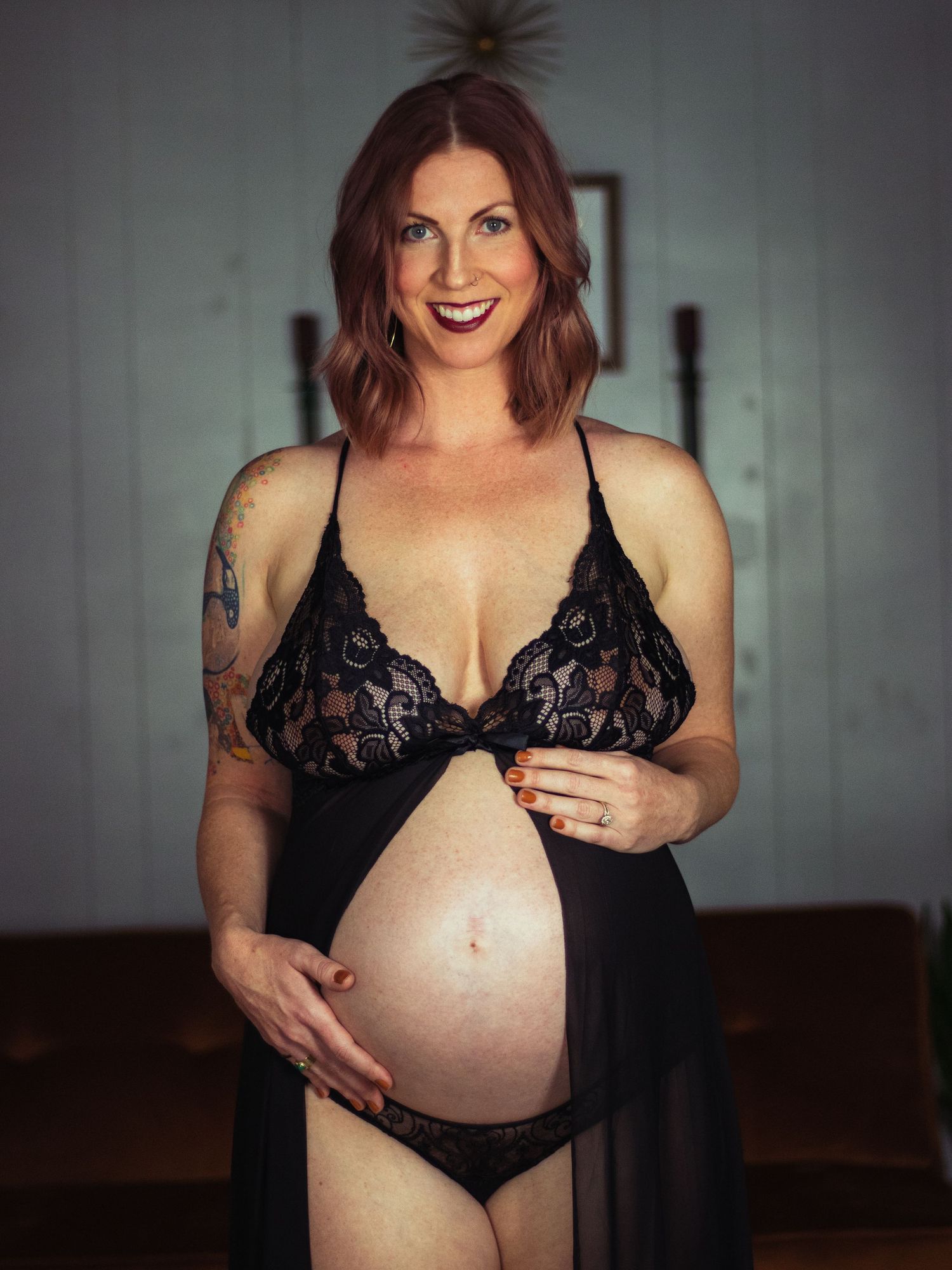 Artistic pregnancy photo featuring dark lace lingerie and natural indoor lighting.