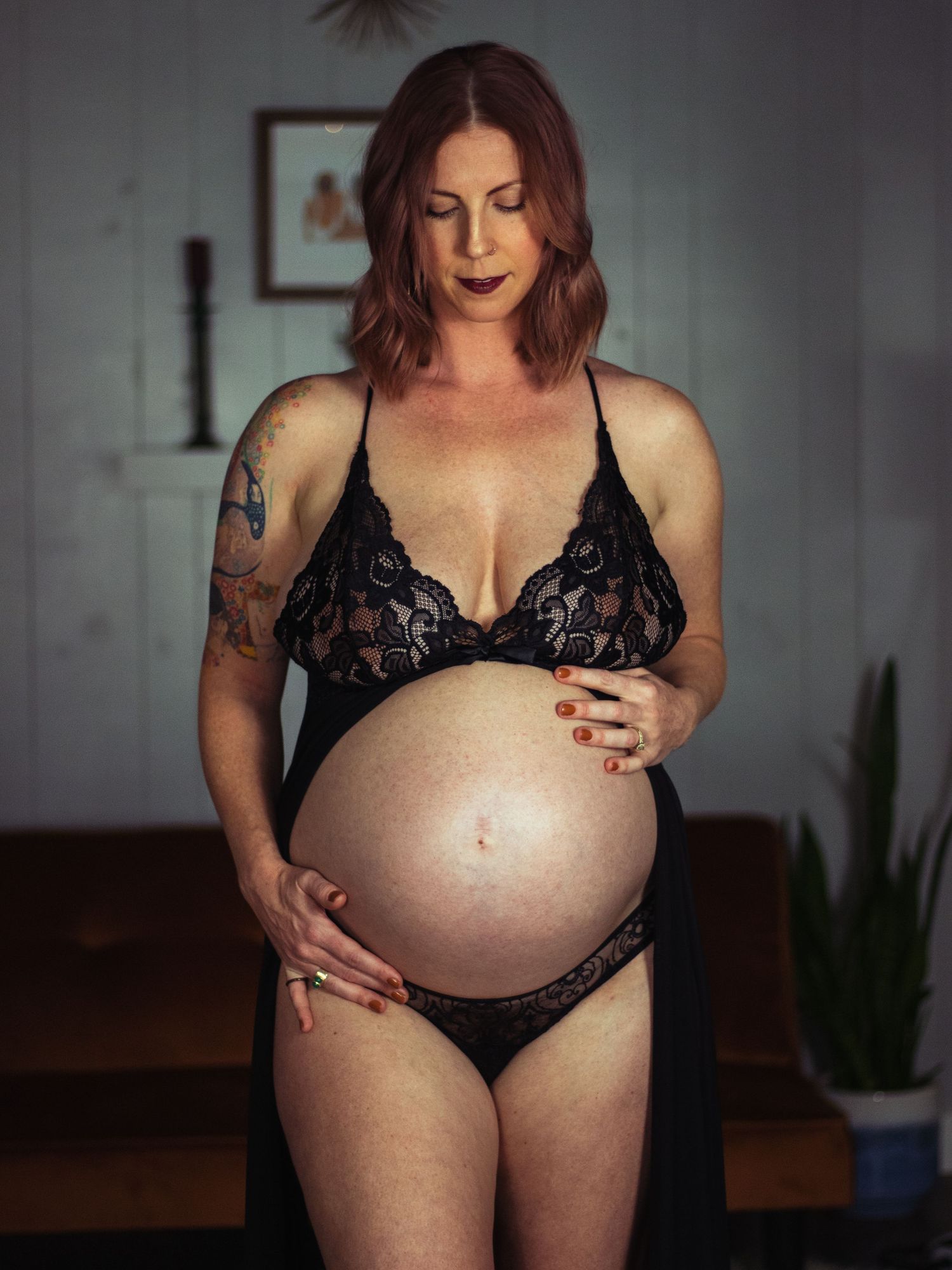 Intimate maternity portrait in black lace lingerie showing pregnant belly in dim lighting.