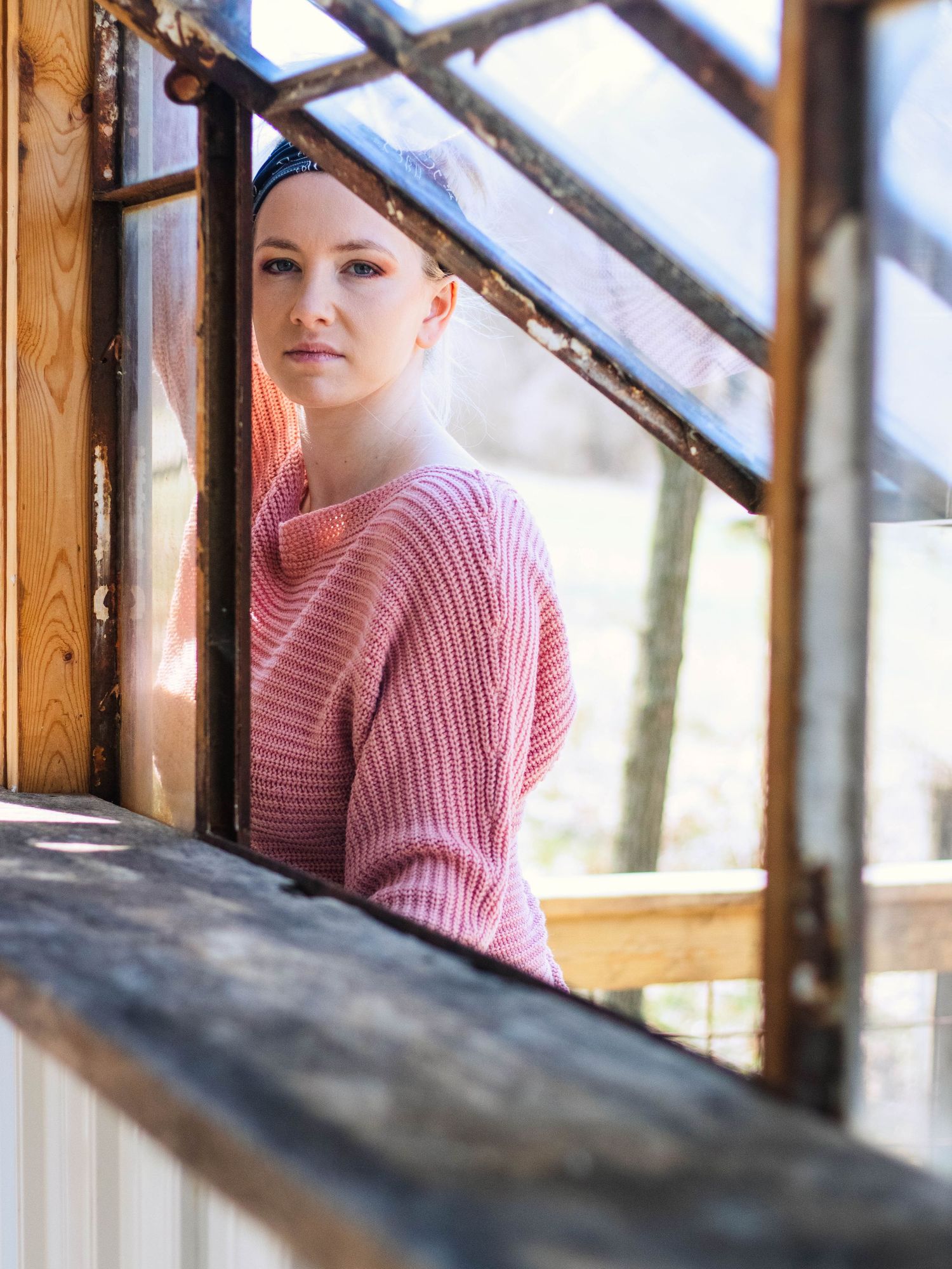 Portrait of figure in pink knit sweater by rustic wooden window frame.