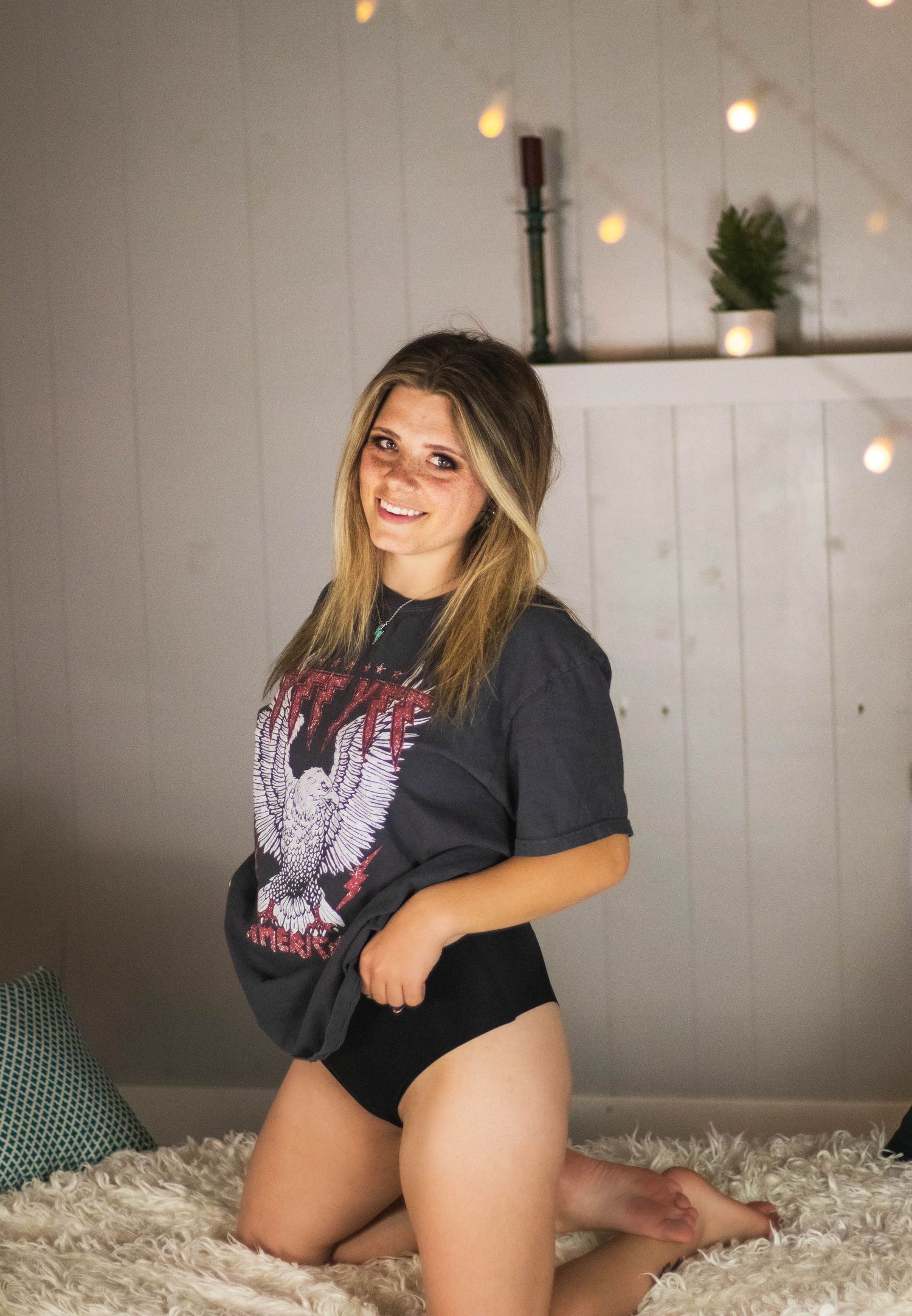 Portrait in casual rock t-shirt against white wall with string lights.