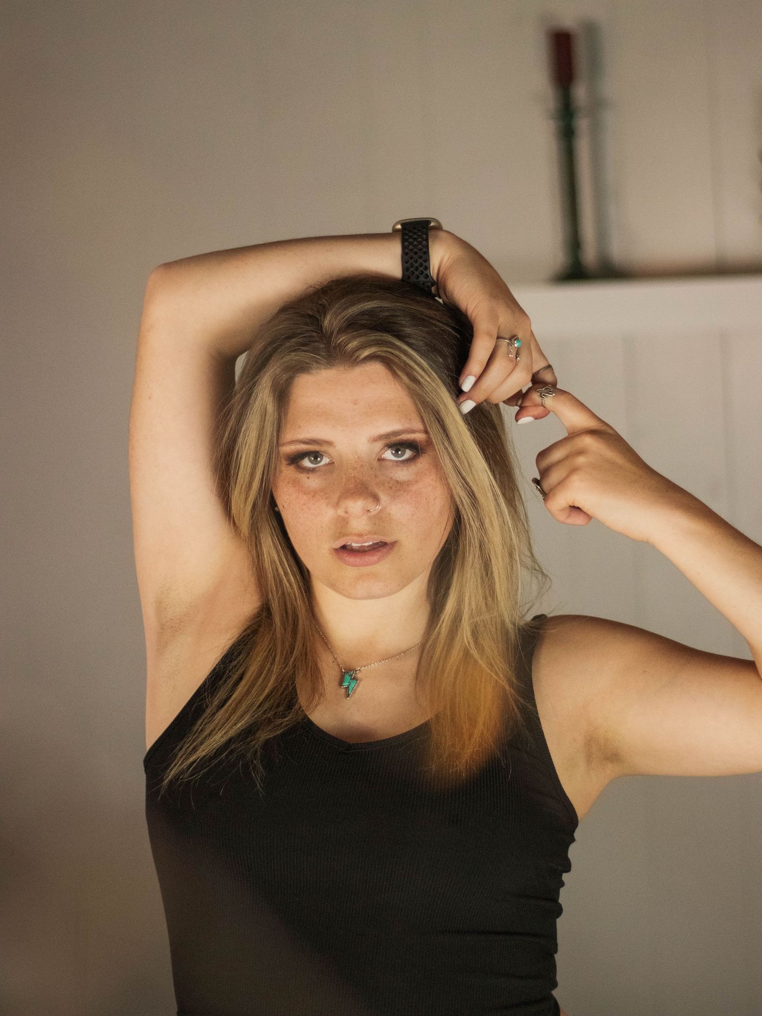 Portrait with raised arms in black tank top against light background.