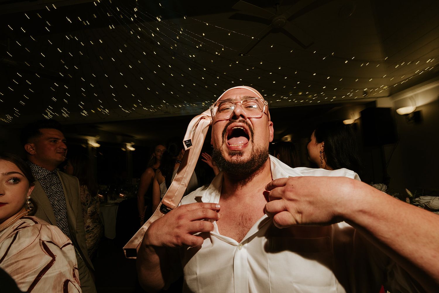 Energetic party guest shouting with excitement under sparkly ceiling lights.