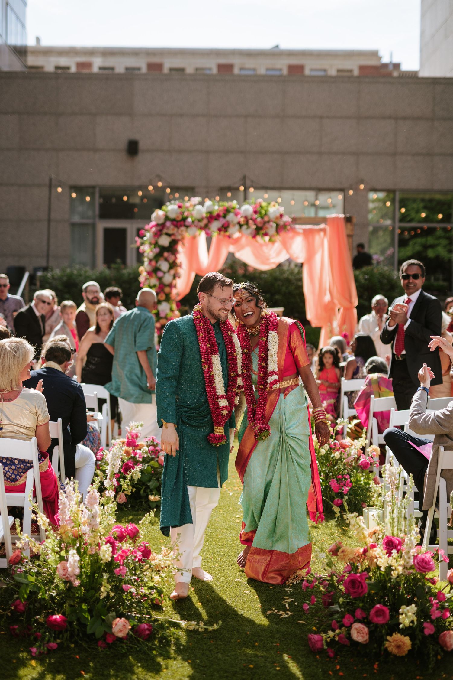 South Asian wedding at The Logan Hotel in Philadelphia, with the couple walking down the aisle in vibrant attire under a floral mandap.
