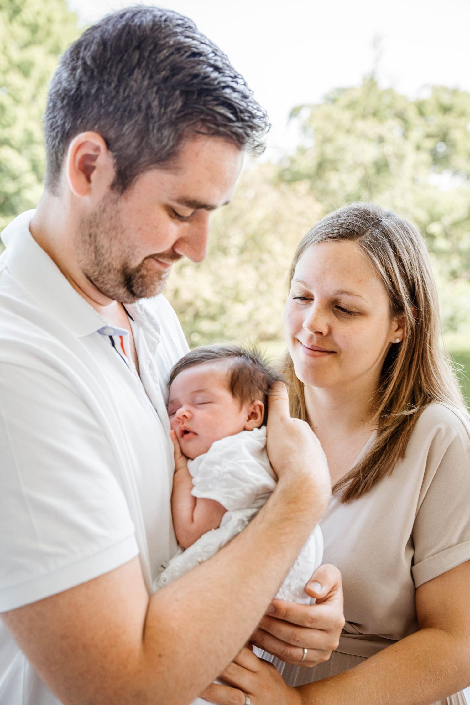 Intimate family portrait outdoors with newborn baby in soft natural lighting.