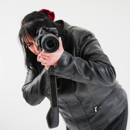 Photographer in black leather jacket shooting with professional DSLR camera.