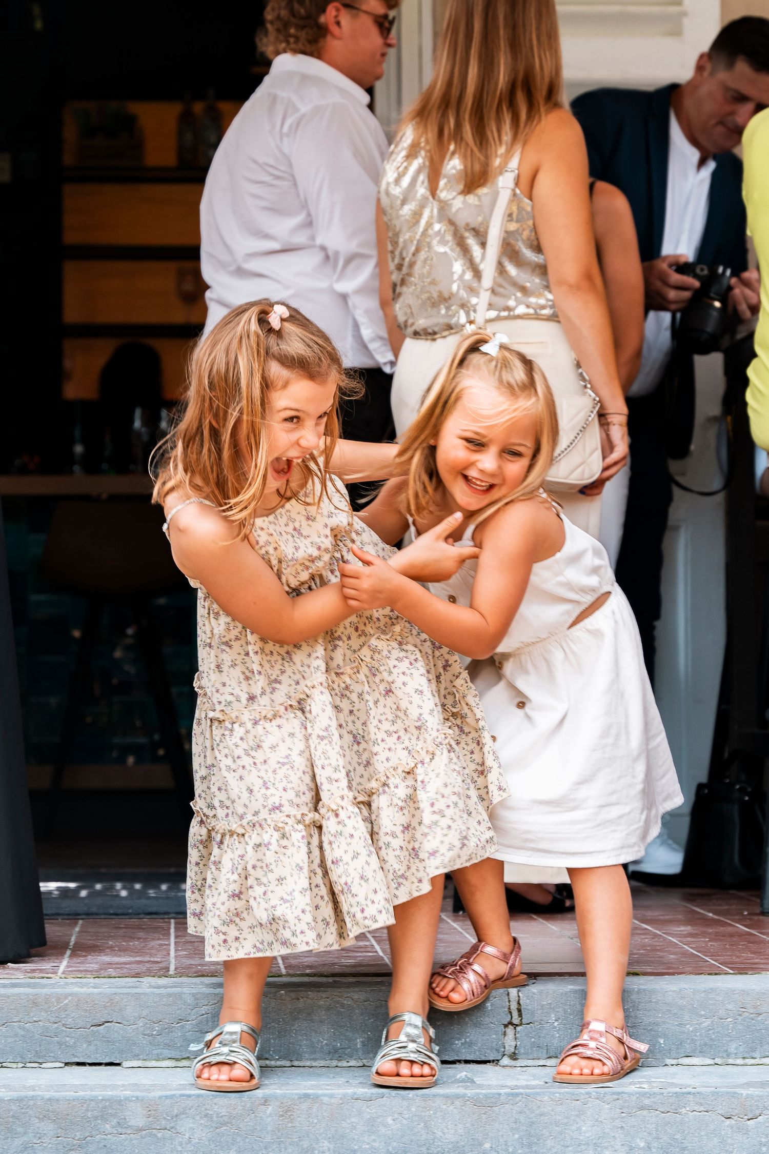 Two young girls in matching sparkly dresses laughing together at a wedding.