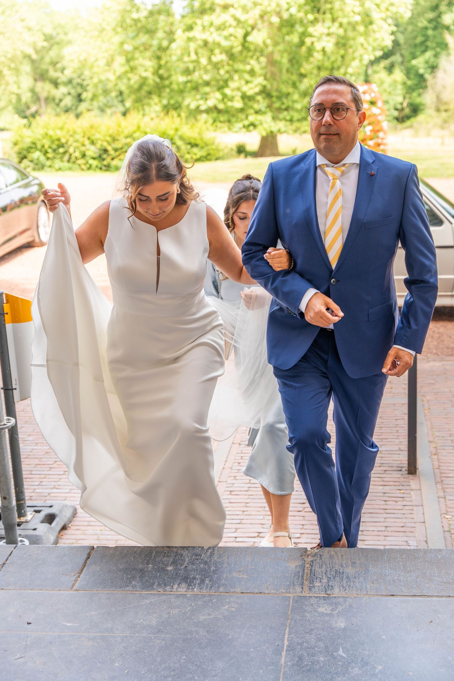 Wedding party ascending stone steps with person in navy suit and white dress.