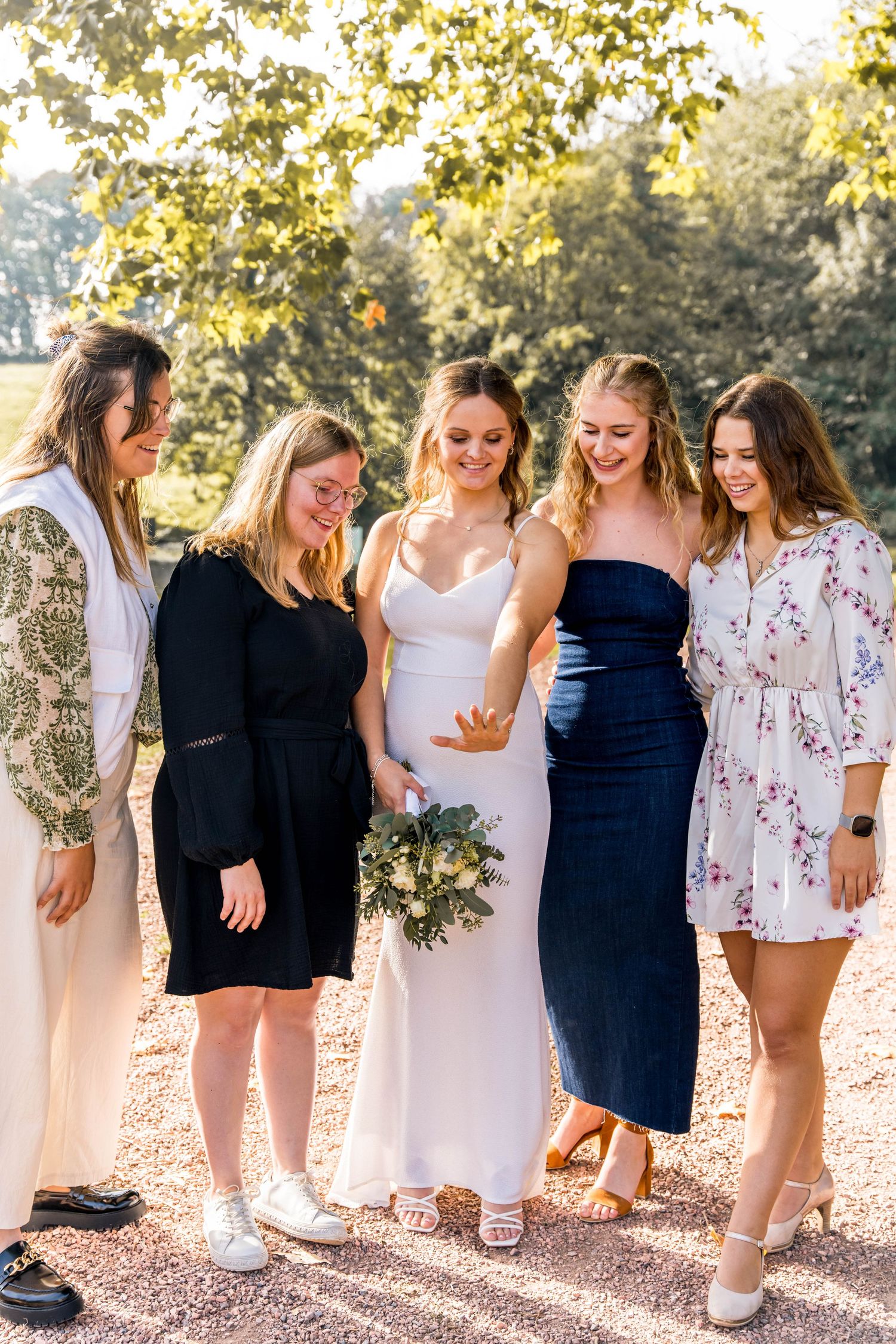 Group of women in assorted dresses gathered on garden path during wedding.