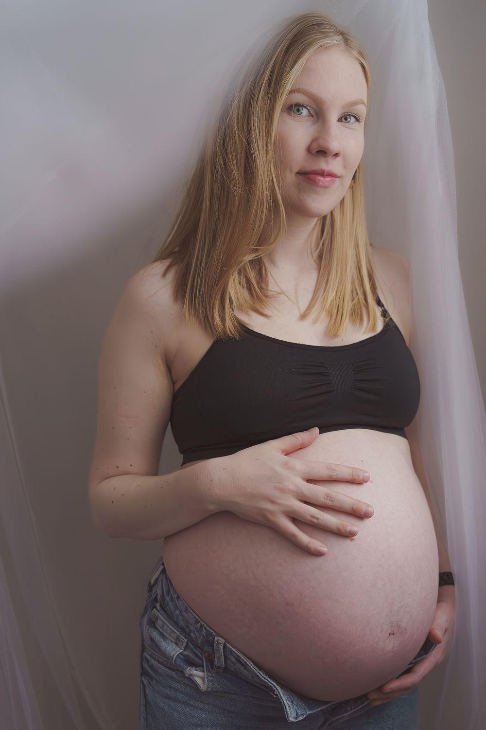 Maternity photo showing pregnant woman in black top against light background.