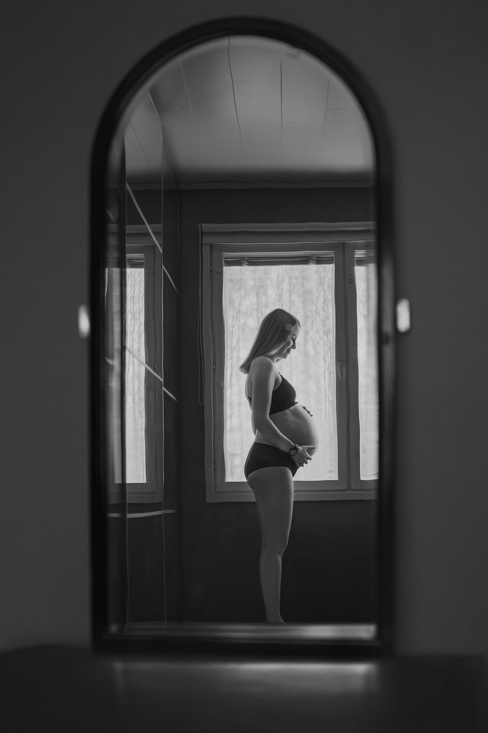 Silhouette of pregnant woman standing by window in black and white photograph.