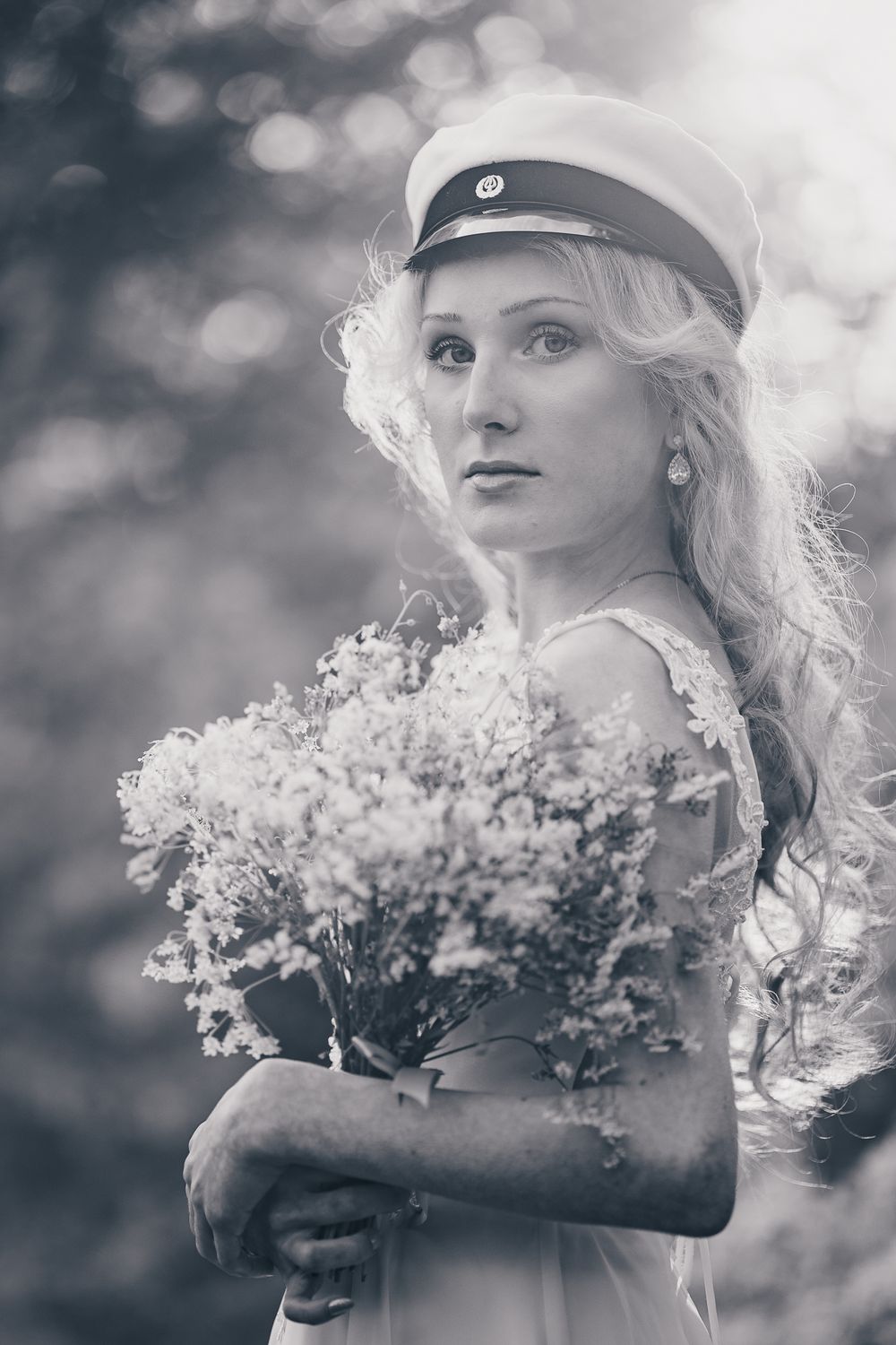A dreamy black and white portrait of someone in a nautical cap holding delicate baby's breath flowers against a soft bokeh background.