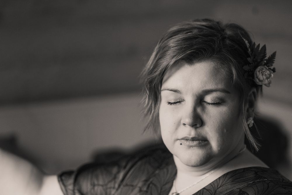 A black and white portrait showing a person with eyes closed and a small floral hair accessory.