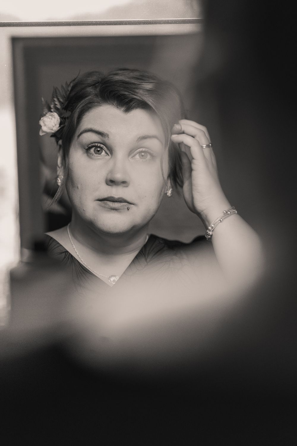 A vintage black and white portrait photograph showing a person wearing a floral hair accessory and bracelet looking up pensively.