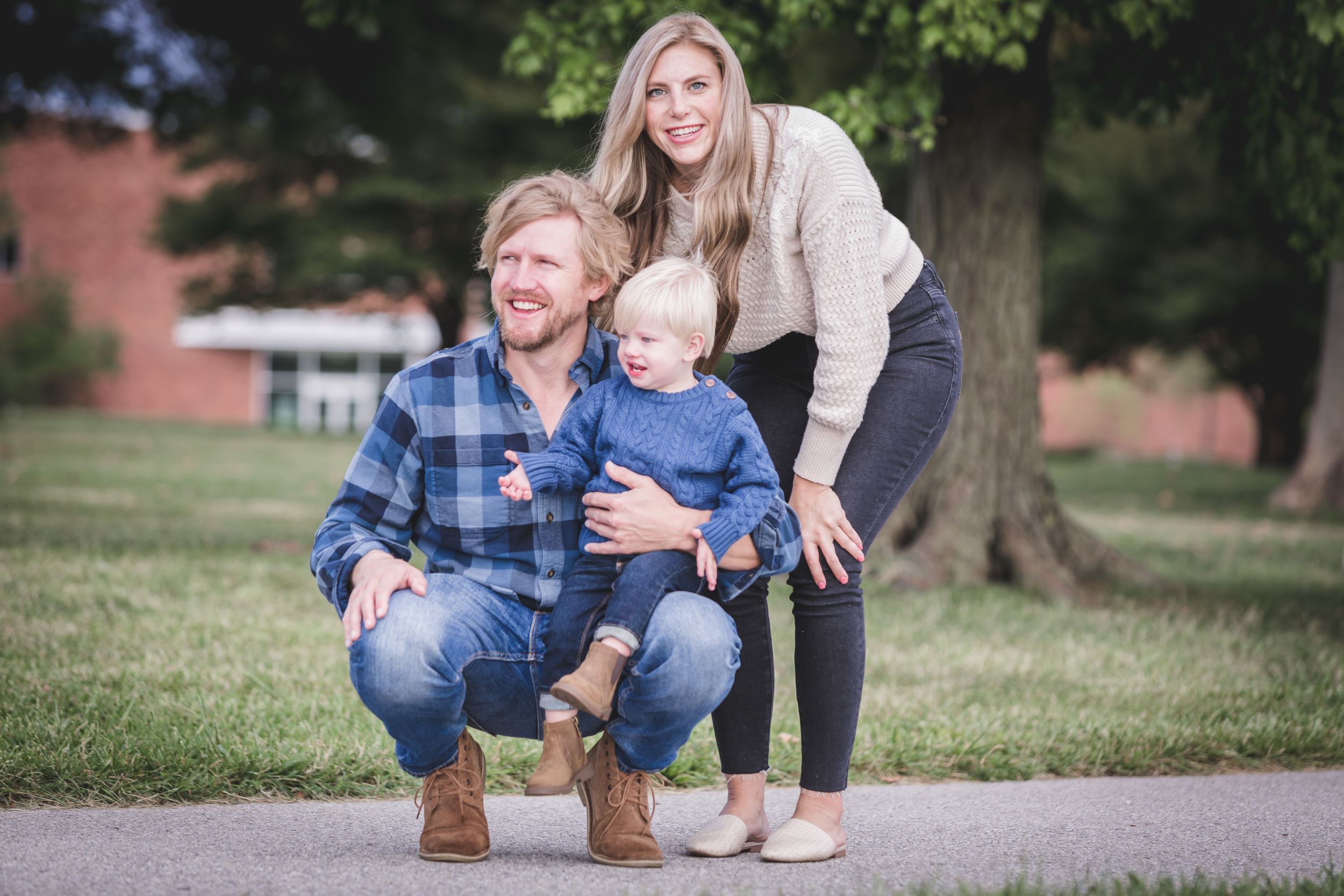 Father holding his baby son with the mother standing beside them outdoors.