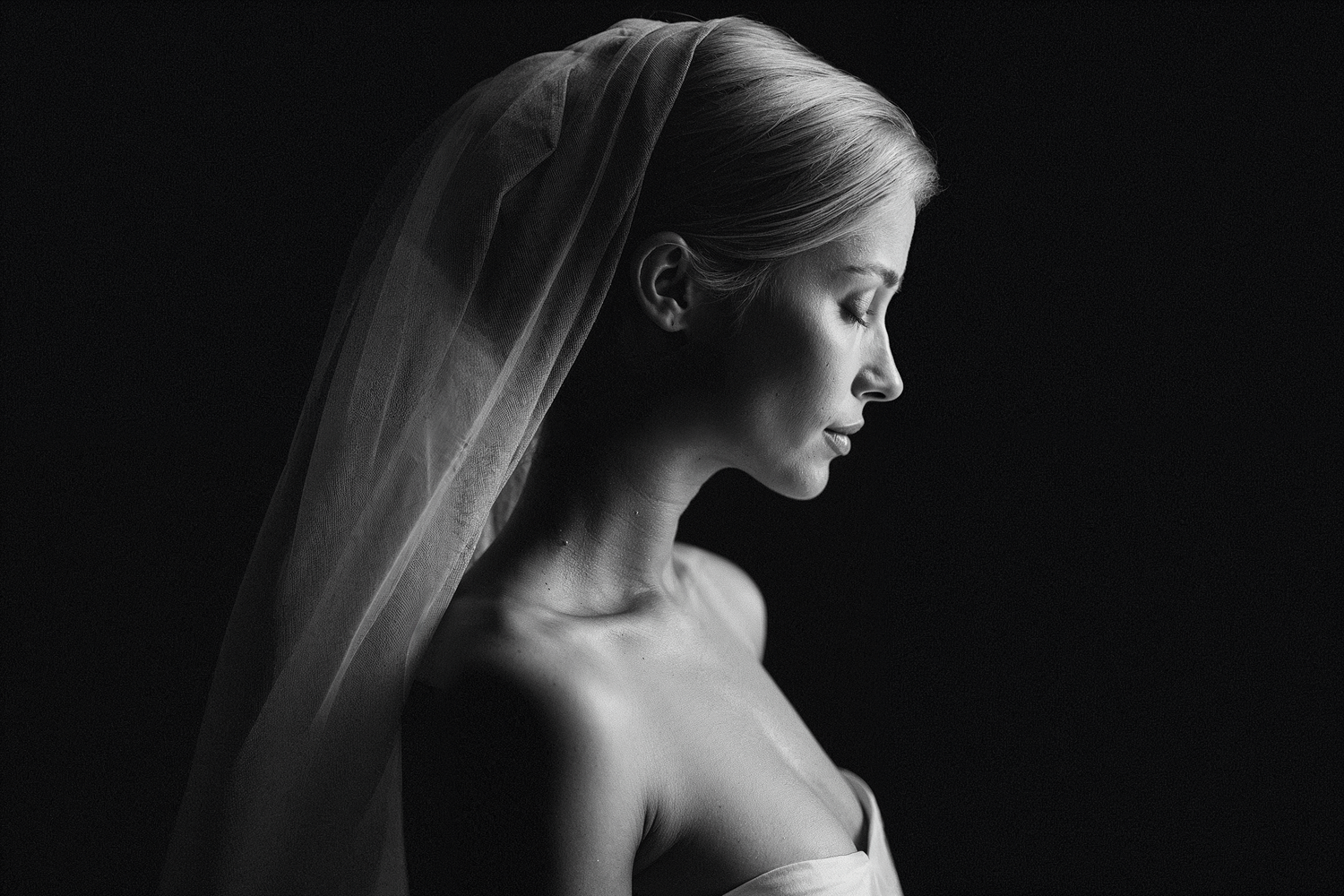 A dramatic black and white side profile with a flowing white veil creating an elegant bridal portrait.