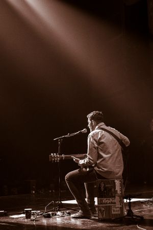Solo acoustic guitarist in black and white with stage lighting illuminating from the top left.
