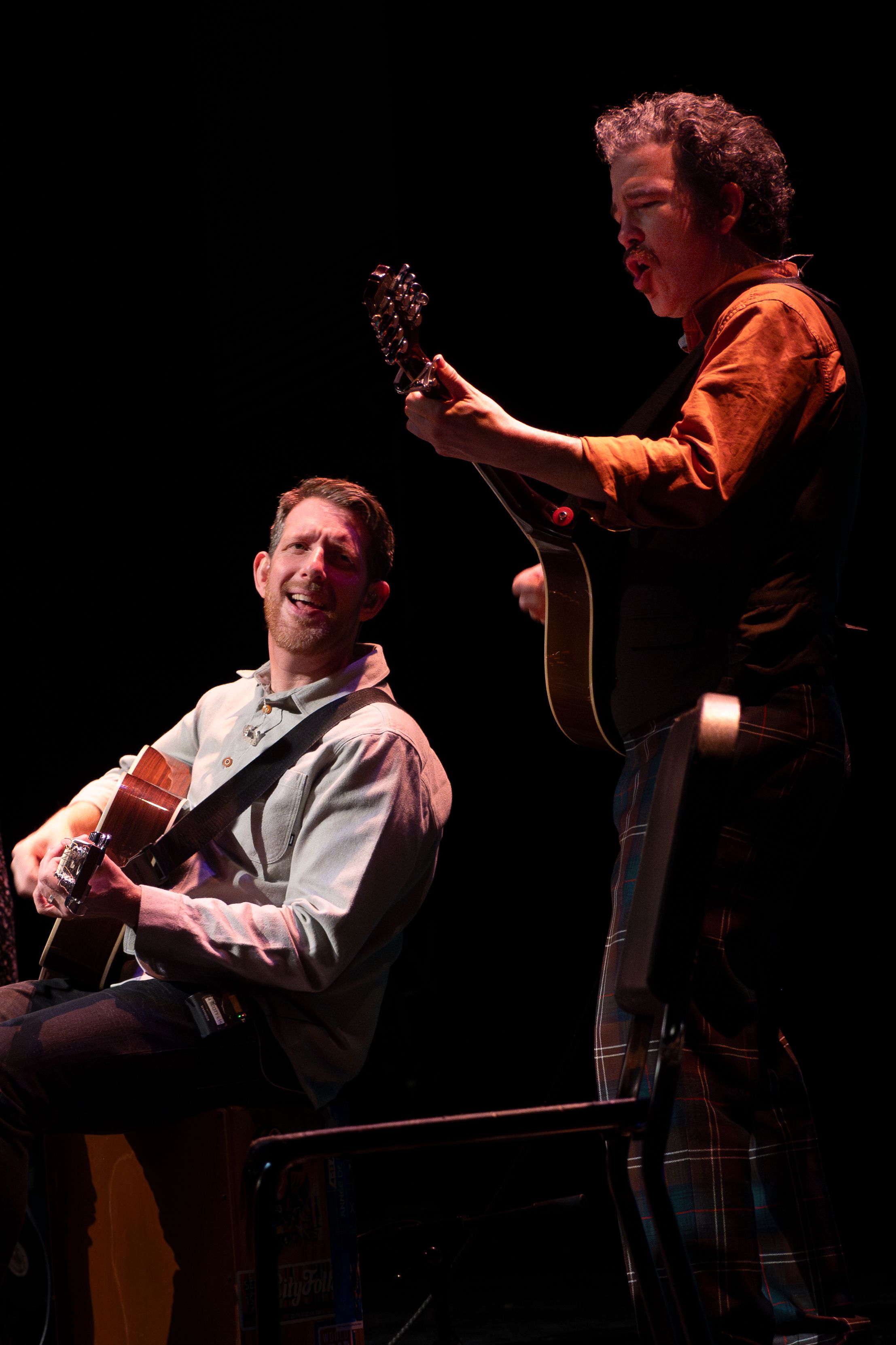 Two acoustic guitar players performing. One sitting and one standing.
