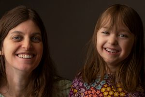 Two people share joyful expressions in intimate portrait against dark background.