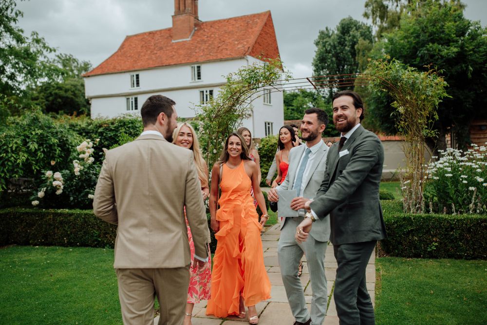 Garden party guests in summer attire socialize on manicured lawn.