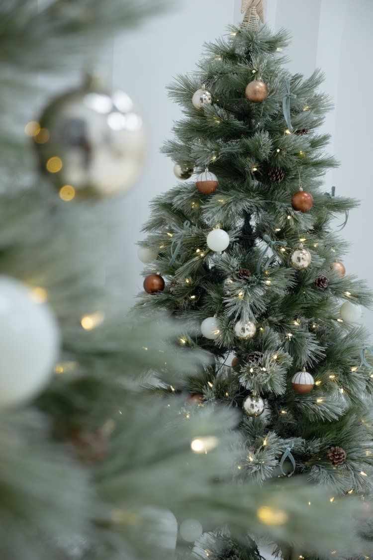 Close-up of Christmas tree decorated with gold and silver ornaments, pinecones and twinkling lights.