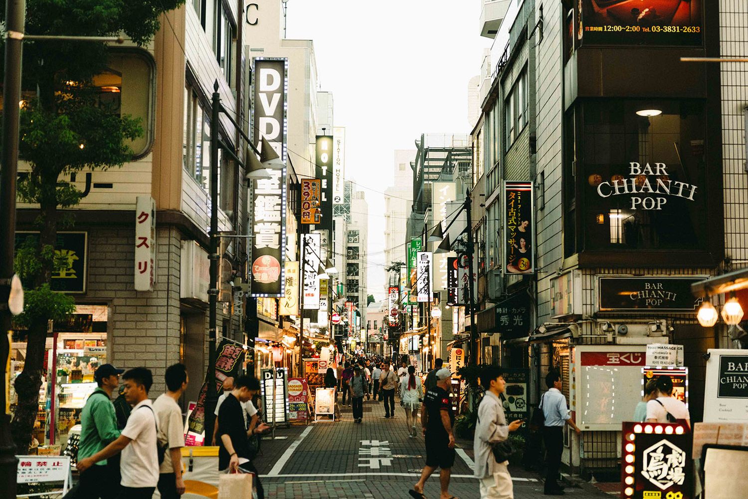 Urban street scene in Tokyo with neon signs, shops and pedestrians walking through a narrow commercial alley.