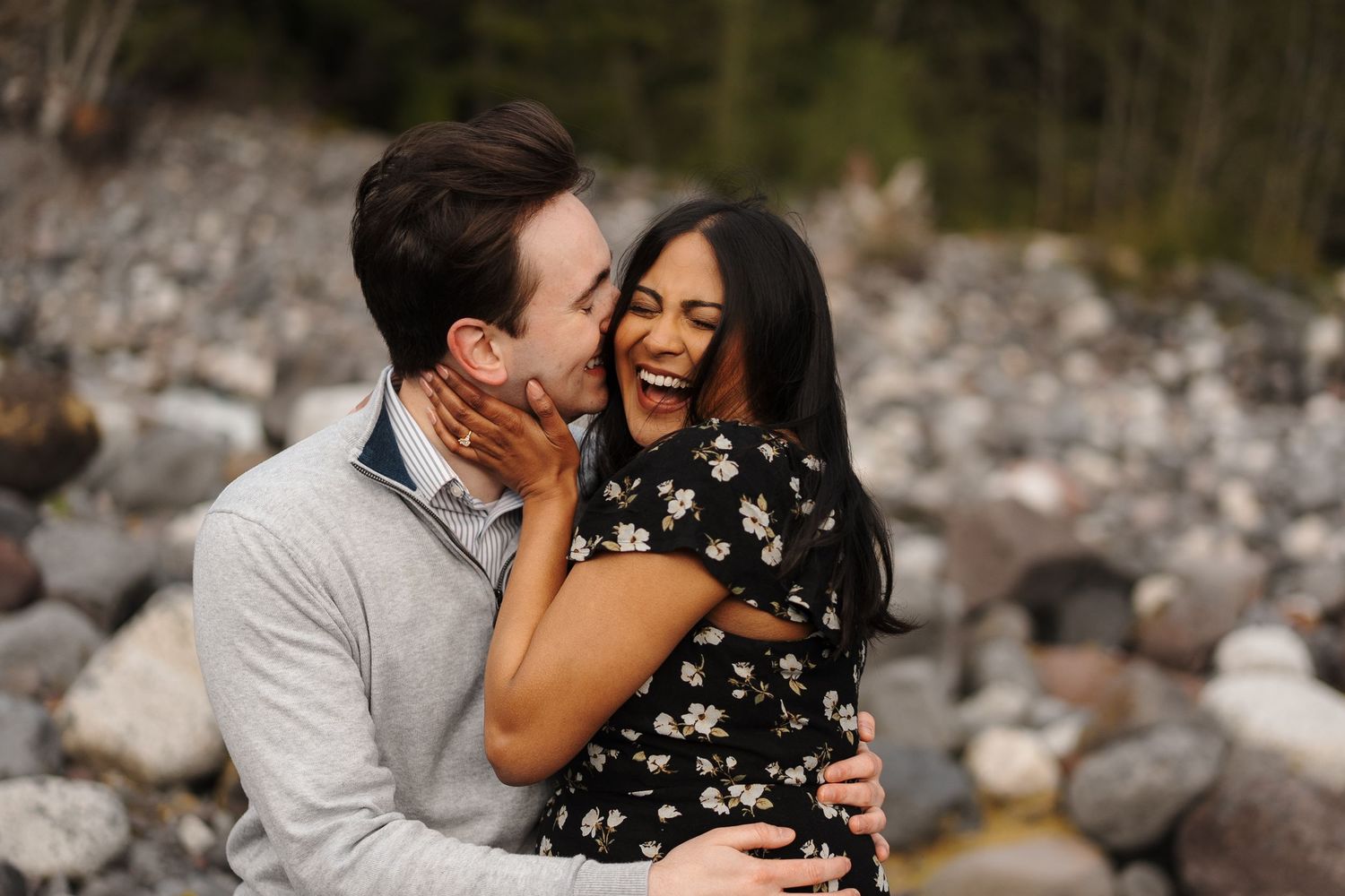 A proposal moment unfolds on rocky terrain with mountains and evergreen forest in the misty background.