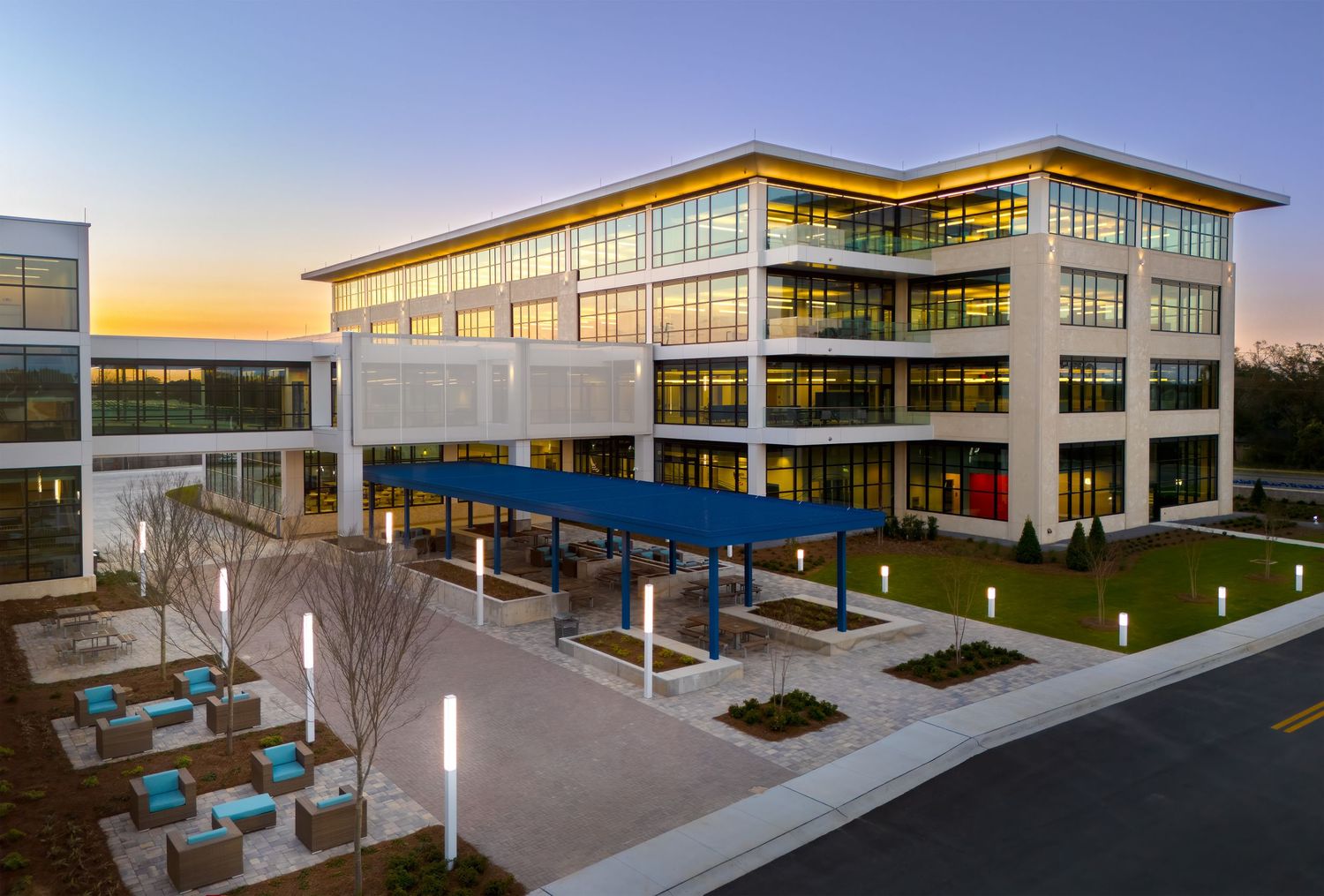 Modern three-story office building with glass exterior and blue covered walkway illuminated at sunset.
