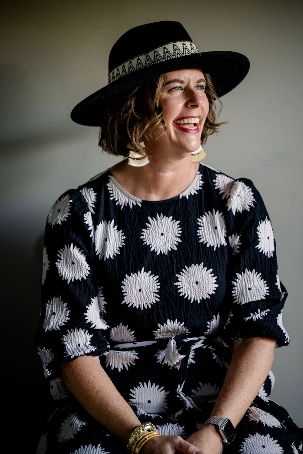 Interior portrait series showing someone wearing a black and white floral print dress with a wide-brimmed black hat.