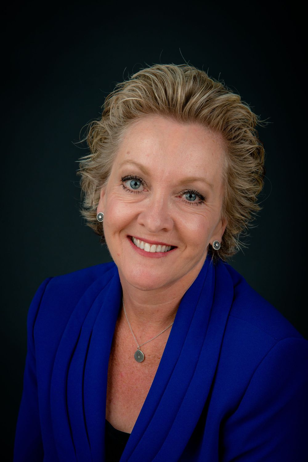 Professional headshot portrait of someone in a bright royal blue blazer against a dark background.