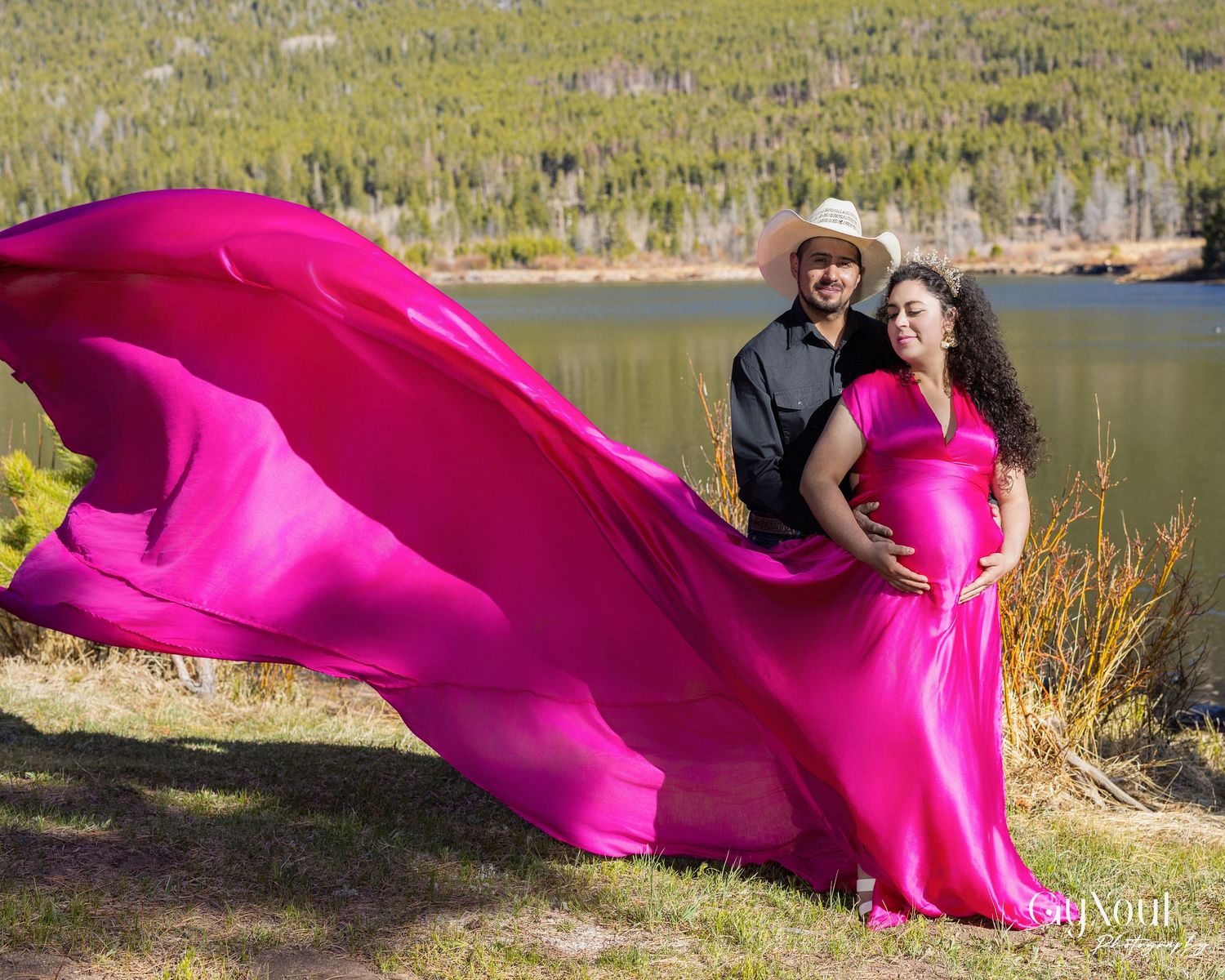 Vibrant hot pink fabric flowing dramatically in the wind against a natural outdoor lakeside landscape.